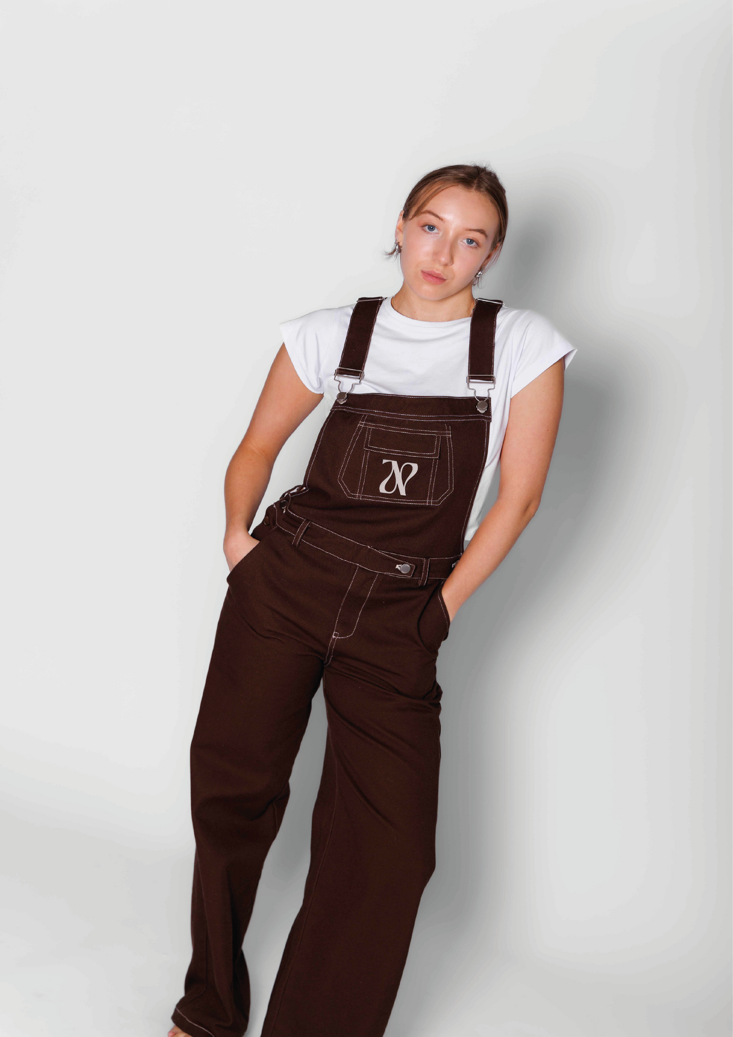 Woman wearing brown oversized dungarees with a knitted top underneath  in a white studio 