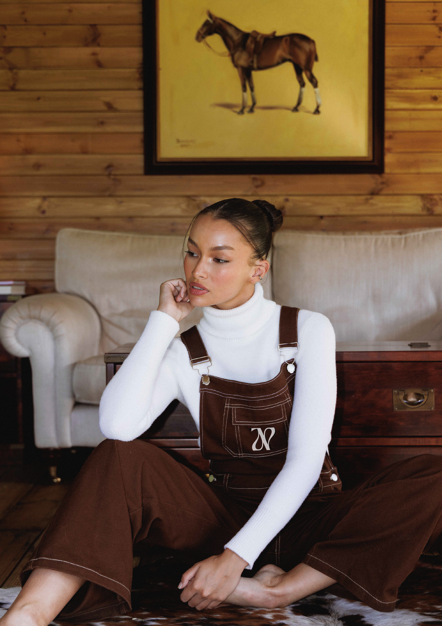 Woman wearing white polo neck with oversized brown dungarees in the countryside 