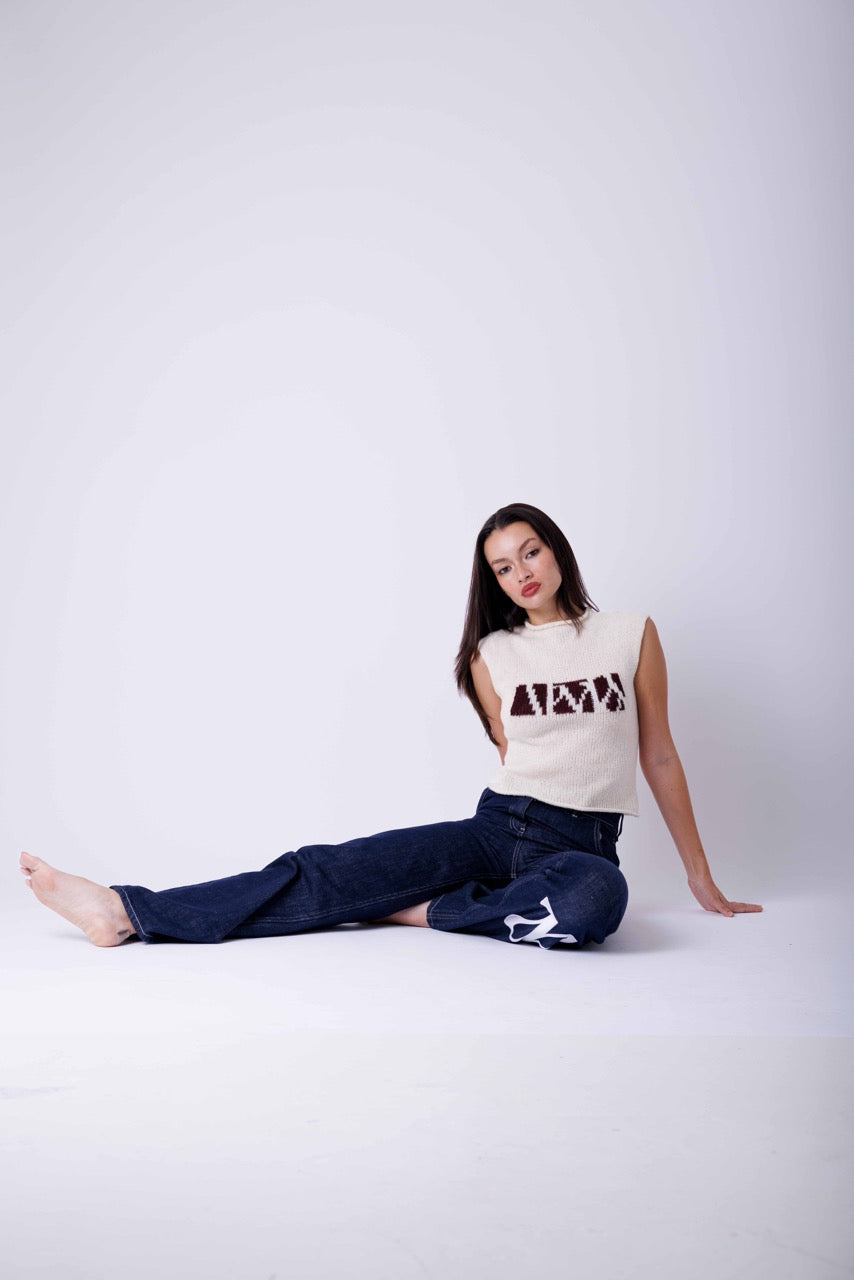 Woman wearing cream knitted top with brown print and dark denim jeans in white studio 