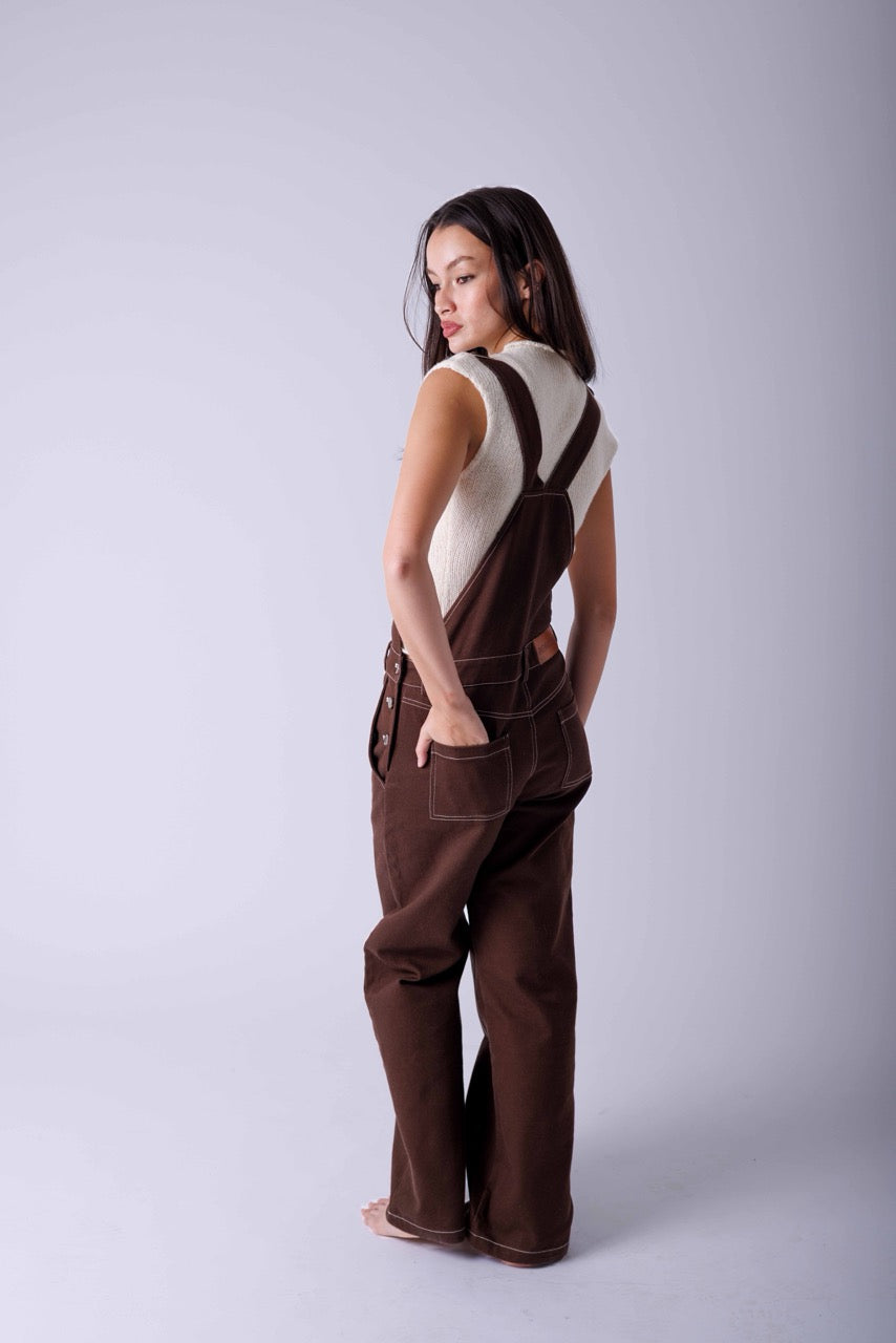 Woman wearing brown oversized dungarees with a knitted top underneath  in a white studio 
