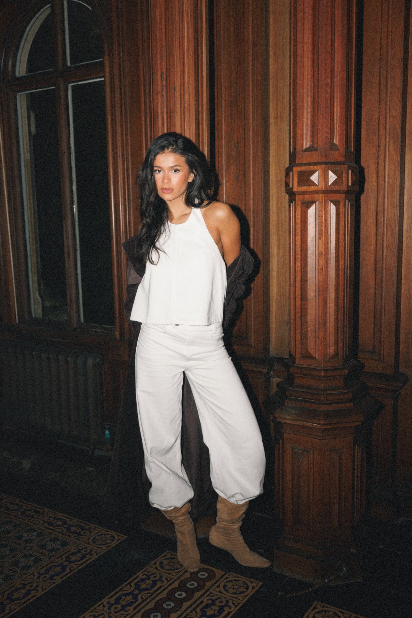 Woman wearing white halter neck top and white wide leg jeans with dark wood background 